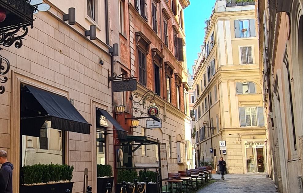 yellow and orange city street in Rome with table and chairs lining the street. 