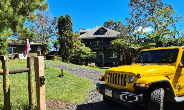 Yellow jeep parked in front of a house and garden. A home stay on Big Island Hawaii.