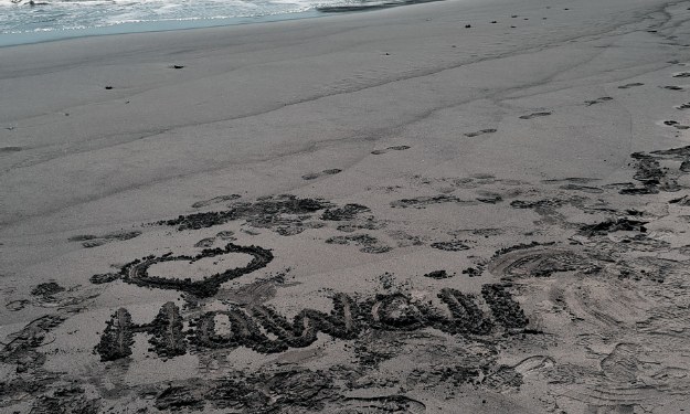 Black sand beach with Hawaii written in and sea.