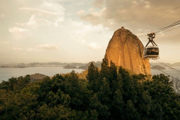 A mountain surrounded by sea and trees. The cable car takes families to the top in Brazil.