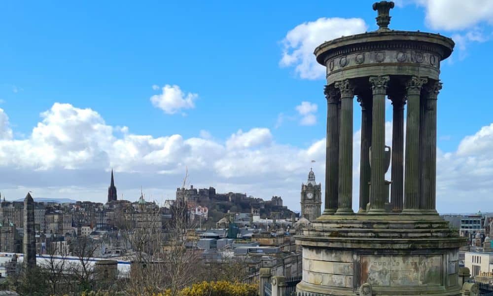 A stone monument with the city of Edinburgh in the distance with blue sky