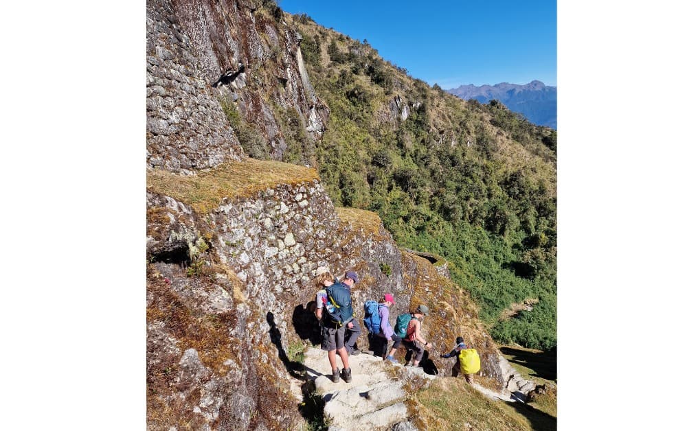 Trekking the Dream family hiking downhill on a narrow path through mountains on the Inca Trail on the way to Machu Picchu.