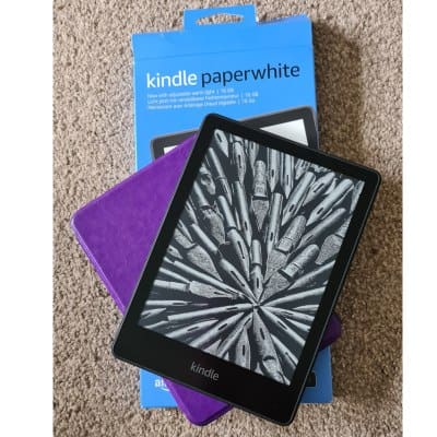 An e-reader stacked on top of a purple cover and blue Kindle Paperwhite store box.