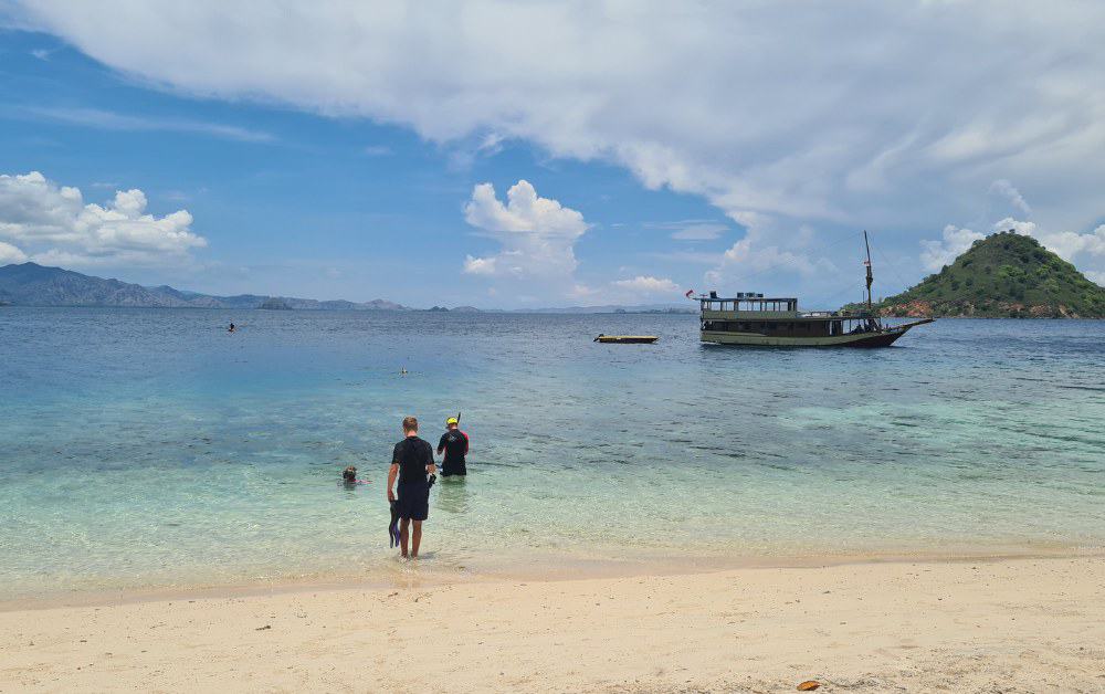 Trekking the Dream family at the shoreline of a yellow beach with a boat in the distance ready to snorkel.