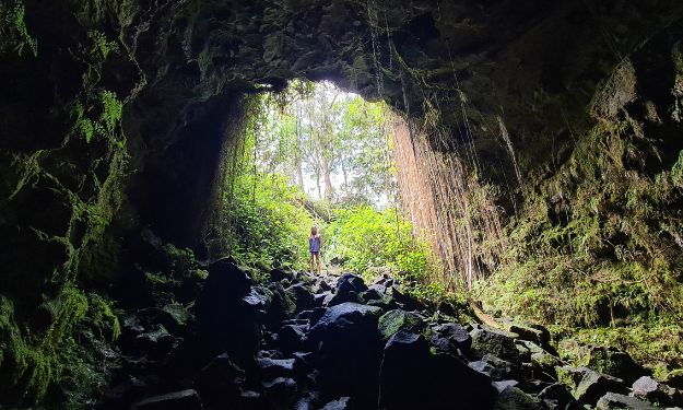 Kid stood in the entrance to a lava cave in Hawaii with daylight coming in from behind.