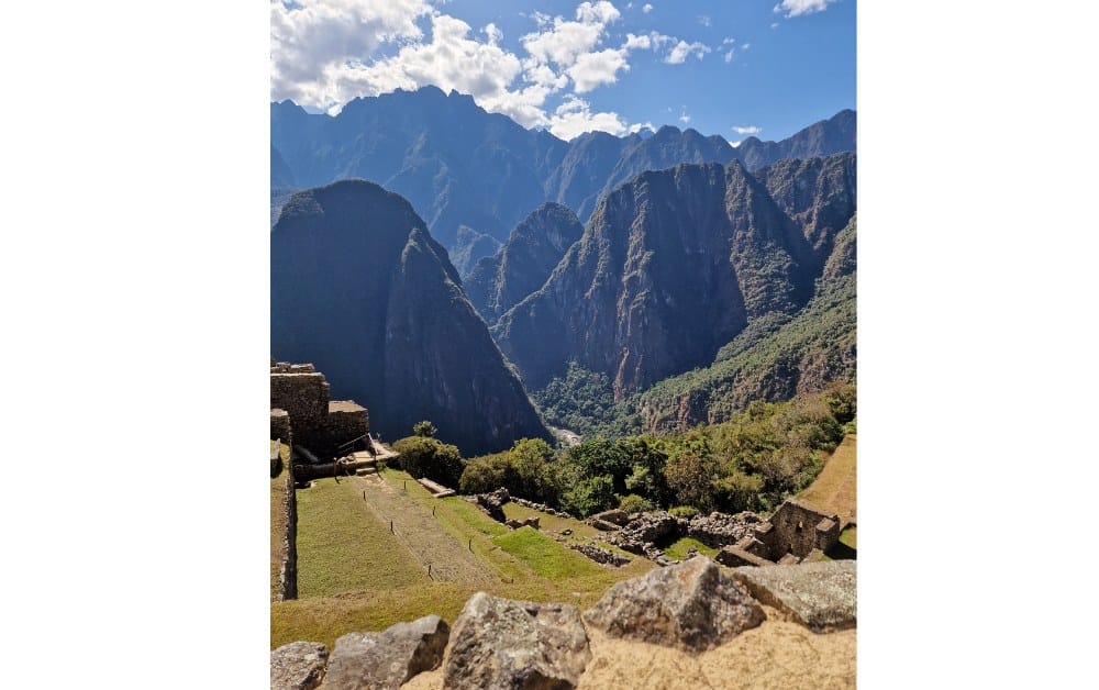 View from a hill containing ruins looking out onto more green mountains. Machu Picchu is a popular destination in Peru with kids. 