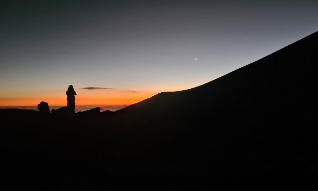 Orange sunset with a silhouette kid on a volcano in Hawaii. A perfect spot for stargazing.