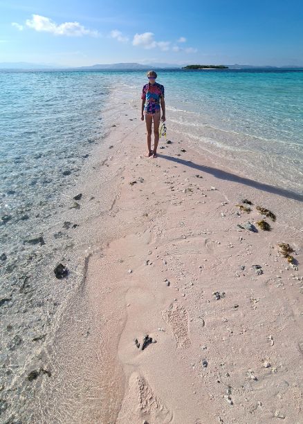 Kid stood on a pink sand beach surrounded by crystal clear sea in Komodo National Park