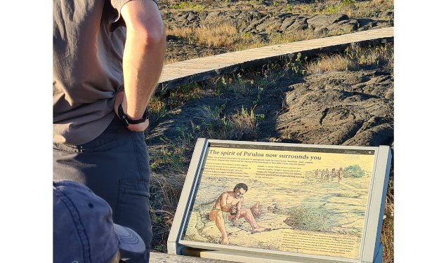 Trekking the Dream Family on a walkway over lava reading a sign about Petroglyphs in Hawaii.