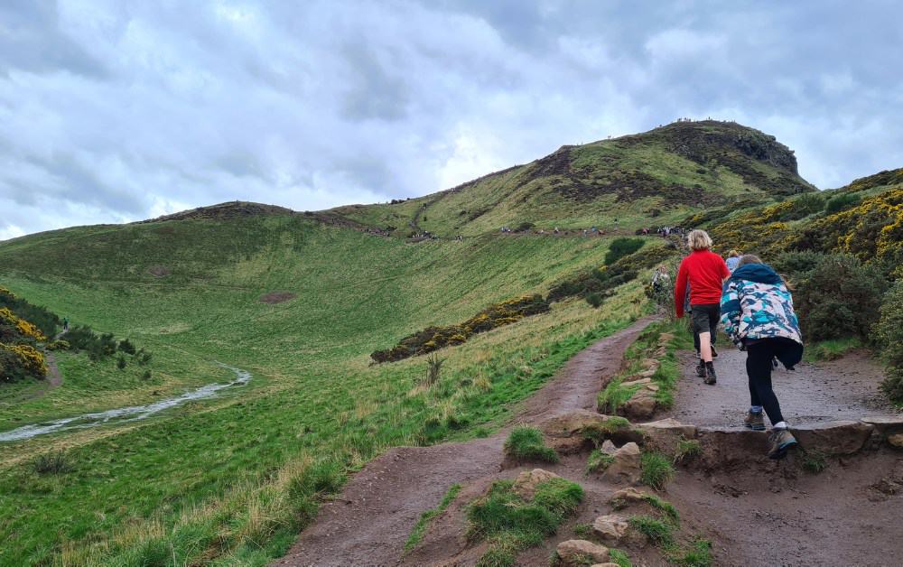 Trekking The Dream kids hiking the trail to Arthur's Seat surrounded by green hills.