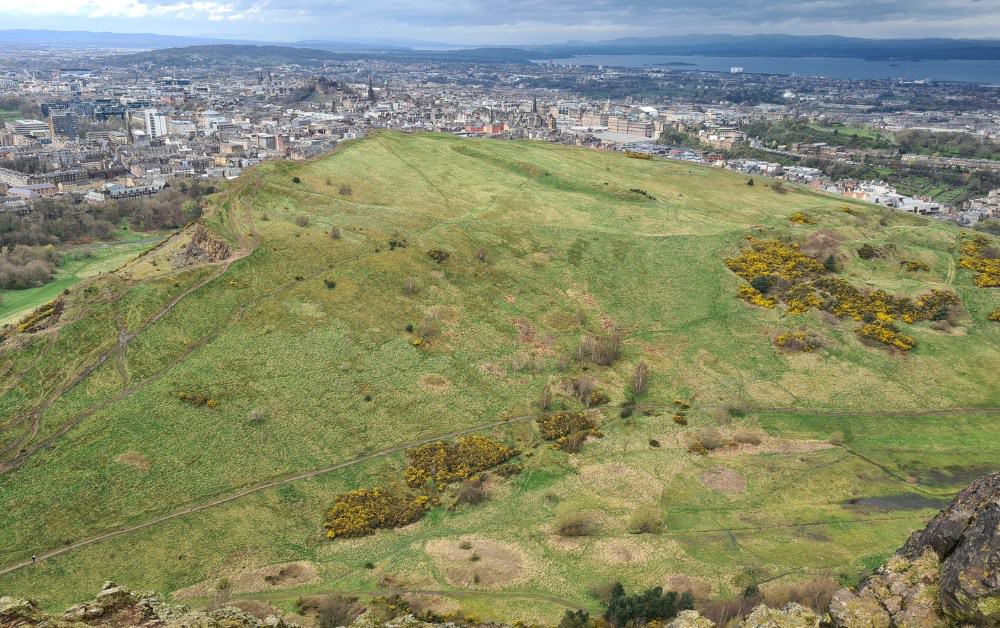 A view from the rocky summit of Arthurs Seat over grass onto Edinburgh.