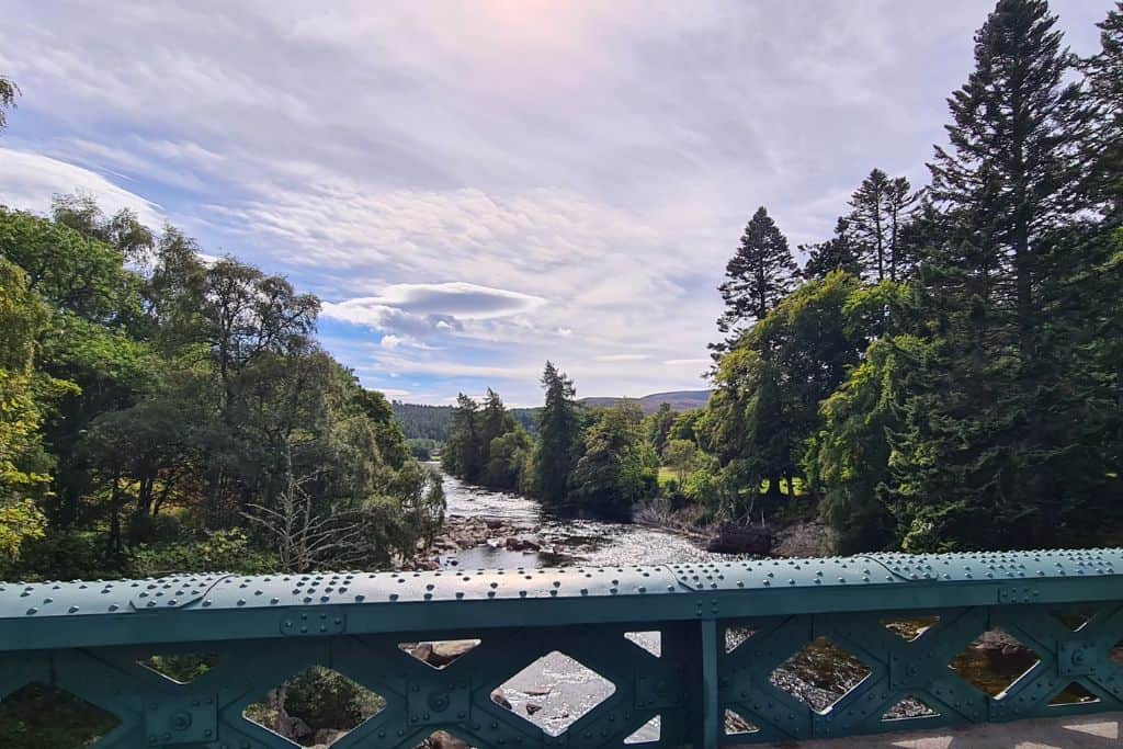 Green bridge over a river lined with green trees. A popular village in Scotland