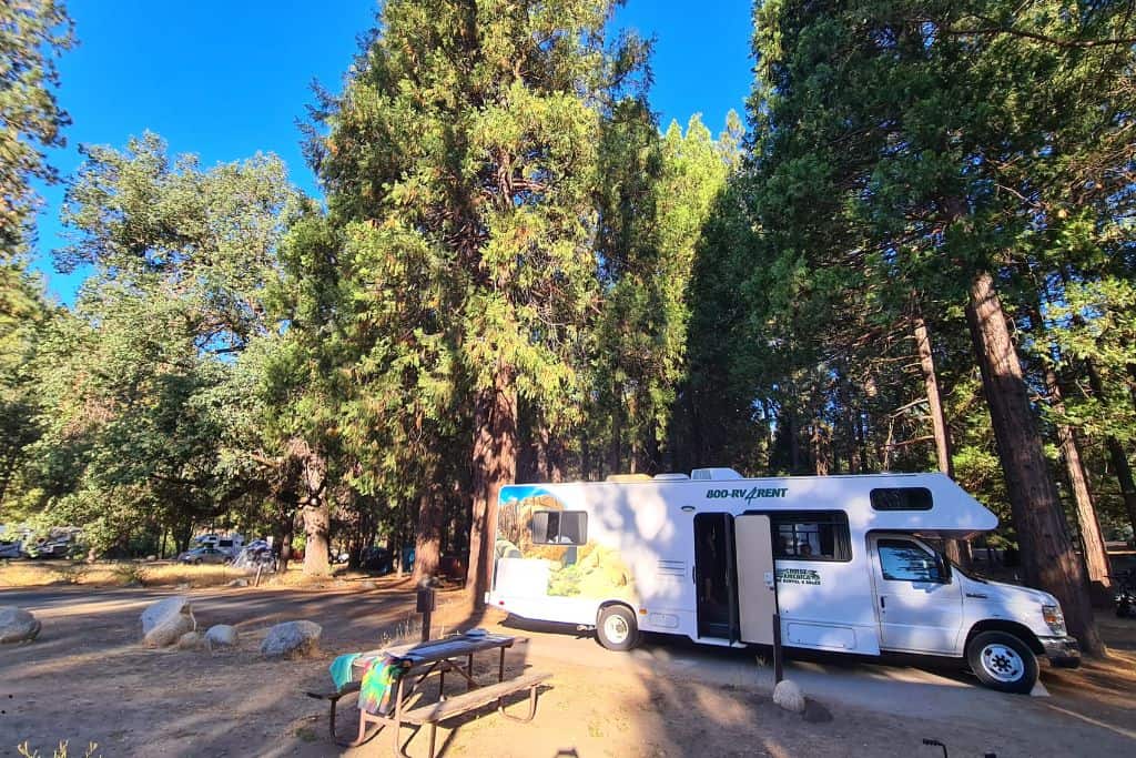 RV in a wooded campsite at sunset on a family road trip.