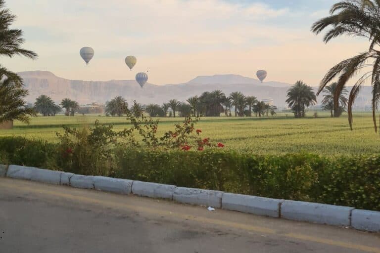 Hot air balloons in the distance surrounded by mountains. A perfect family adventure on a road trip in Luxor, Egypt at sunrise.