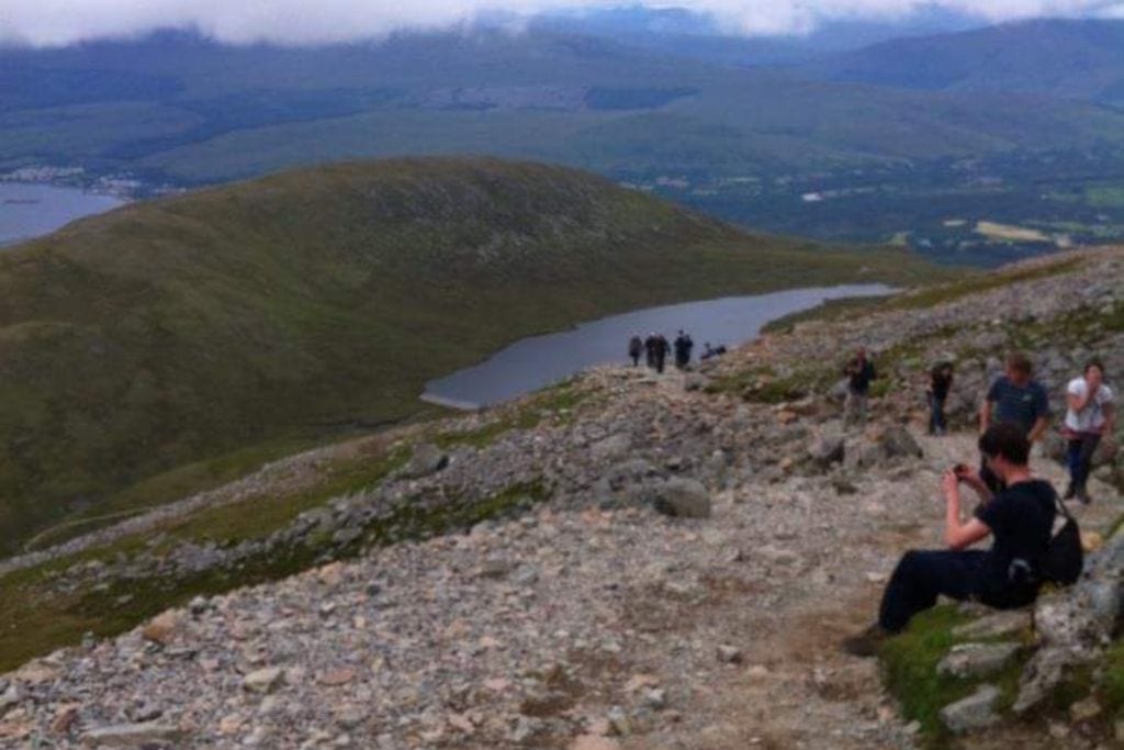 Scenic view from a stony path of a loch and green hills when climbing Ben Nevis