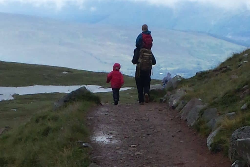 Family walking away on a mountain path towards a pond after hiking Ben Nevis.