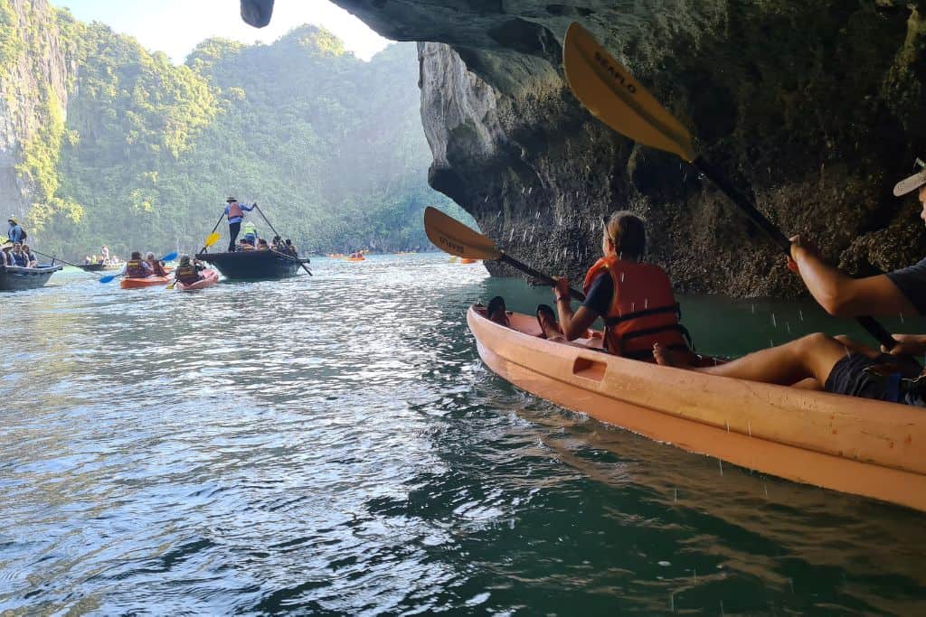 Family kayaking through a cave towards an entrance with cliffs. 