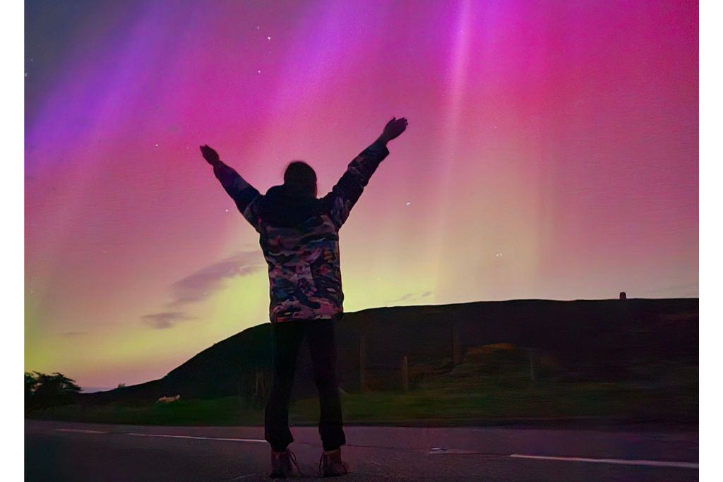 A kid watching coloured beams of light in the night sky. A strong northern light display in Scotland