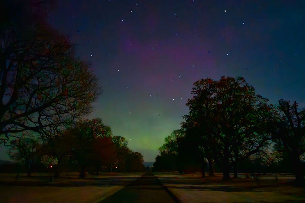 Pink and green northern lights in the night sky at the end of a driveway in Scotland.