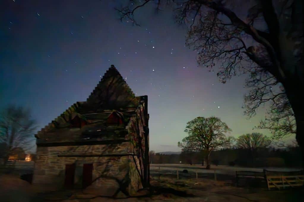 Pink and green colours in the night sky with trees and a building. 