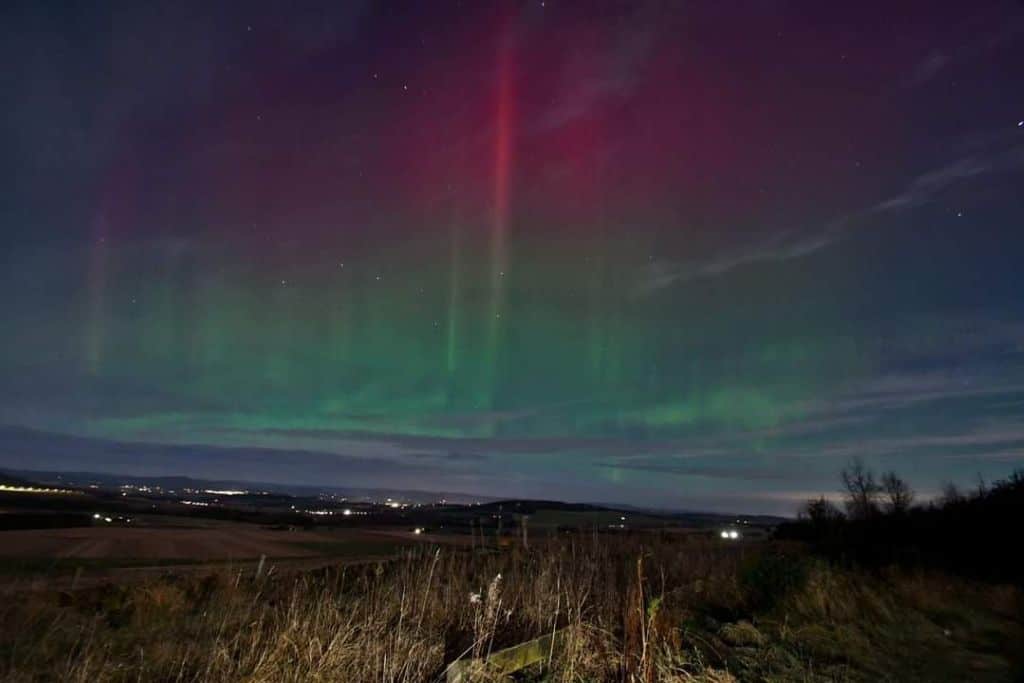 Red and green lights of colour dancing over a field in the October night sky in Scotland.