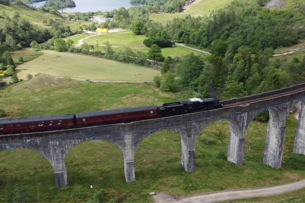 A red steam train cross an arched bridge surrounded by stunning views in Glenfinnan.