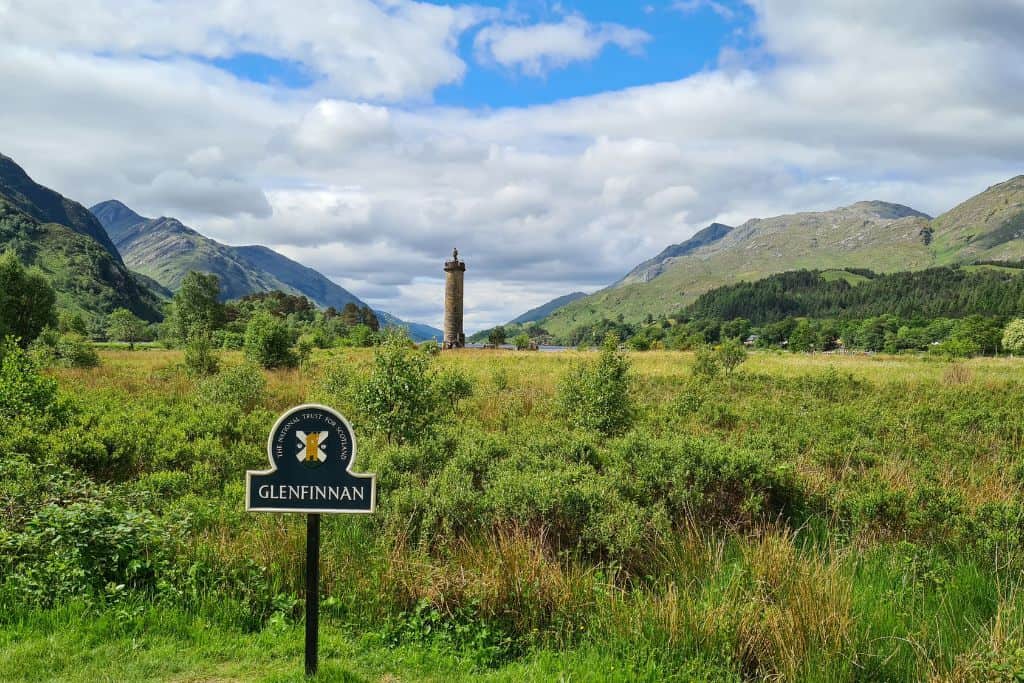 Green landscape with a tower in the distance and a Glenfinnan sign.