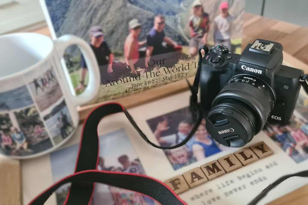 A camera sat on top of a family photo frame, photobook and photo mug - all great options for displaying family travel photos.