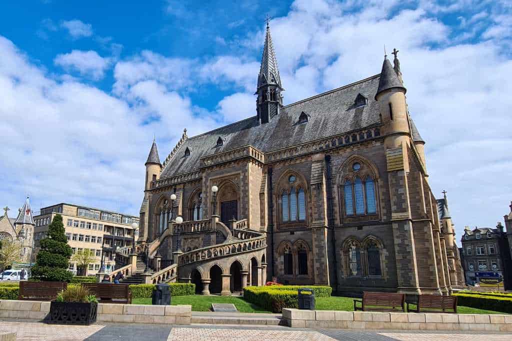 Ornate building with stair entrance to a museum and manicured garden in Dundee.