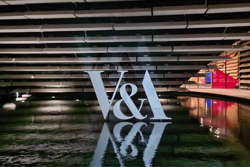 Building with white letters V&A reflected in water.