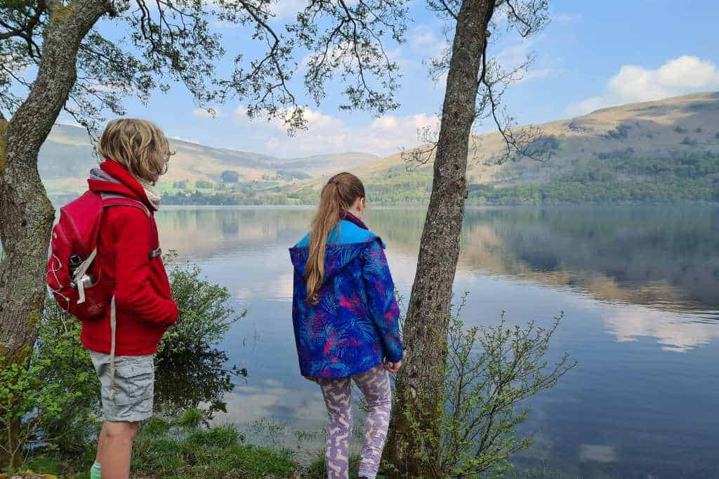 Kids taking a break from walking next to a scenic body of water.