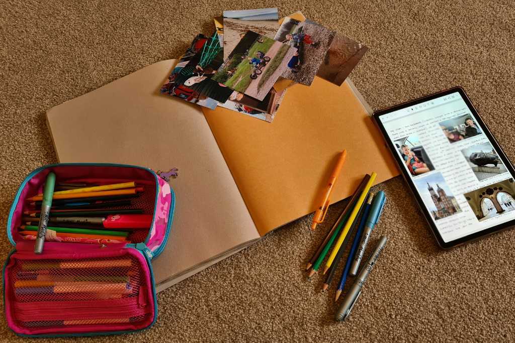 Scrapbook, pens, photos and a digital travel journal on the floor.