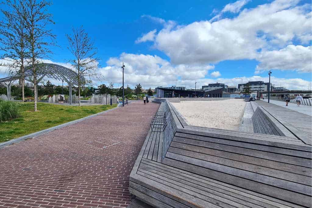 A path lined with benches, sandpit and sculptures with blue sky. An outdoor play area for kids in Dundee.