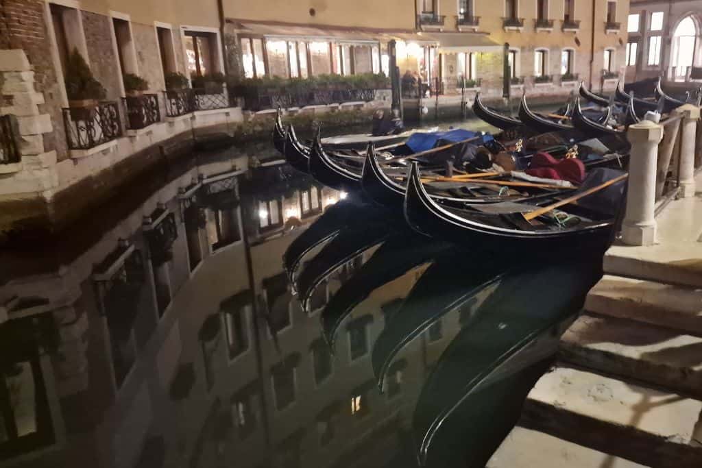 Gondola's floating on a canal lined with houses at night.