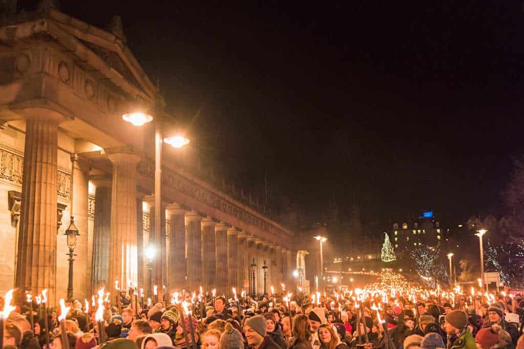 Crowd of people holding lights in a lit street at night as part of celebrating Hogmanay in Scotland.