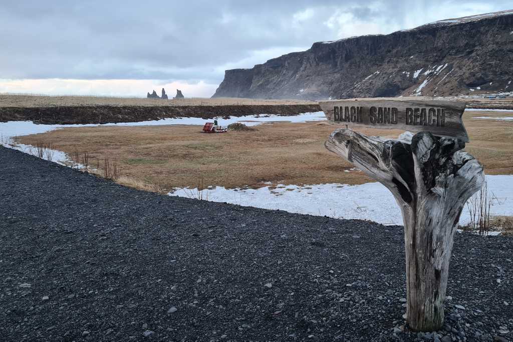 A wooden tree sign stating the direction to Black Sand Beach. This is a reason to visit Iceland.