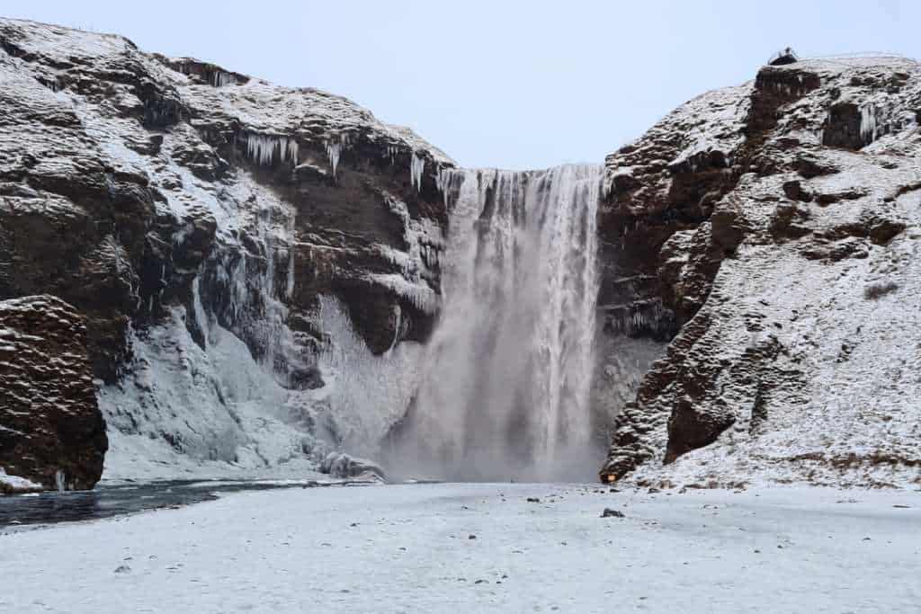 A tall gushing waterfall surrounded by rock, covered in snow on Iceland's South Coast.