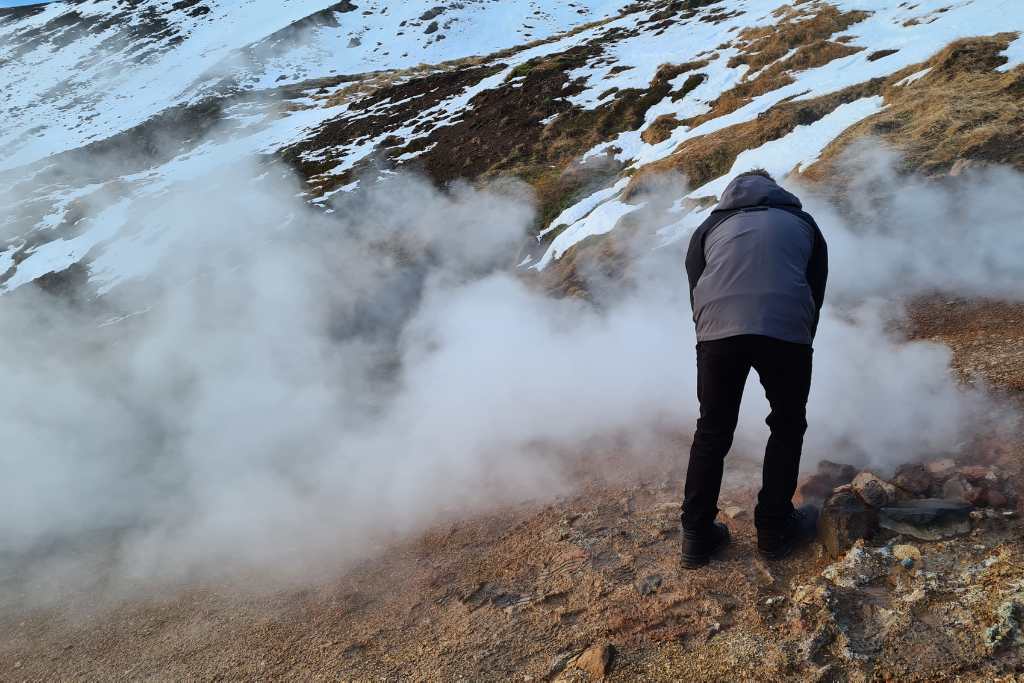 A child looking at steaming rock in a field.