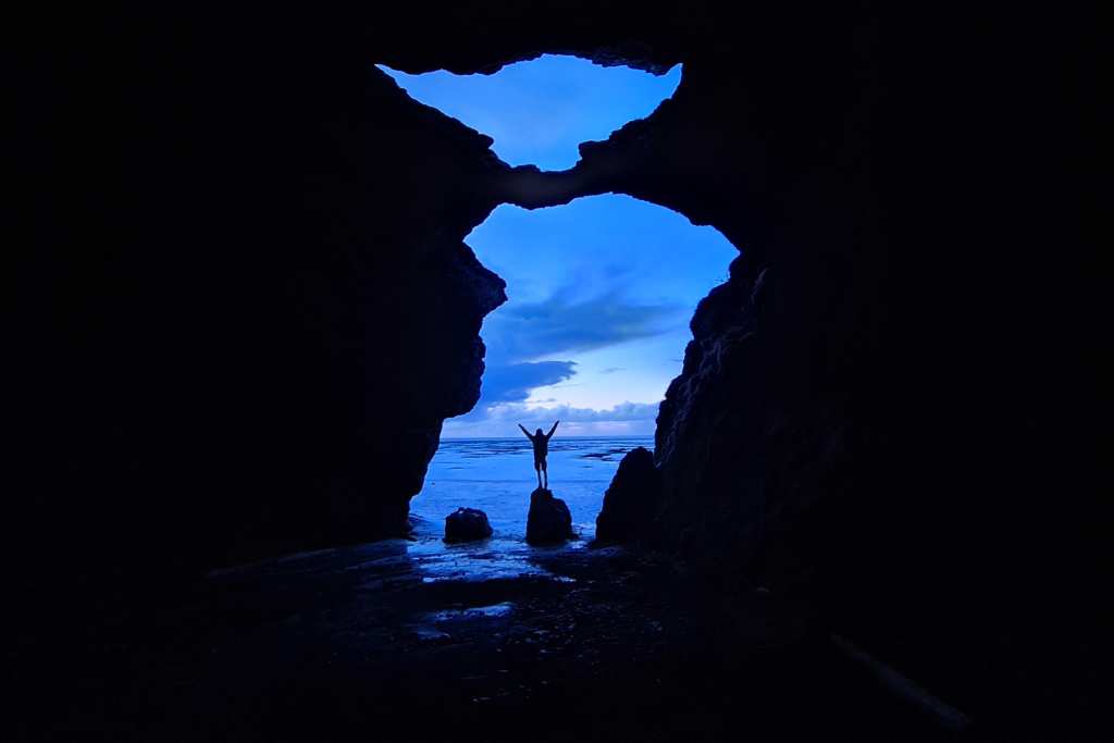 A large shape in a rock creating the entrance to a cave with a kid in the centre in Vik Iceland.