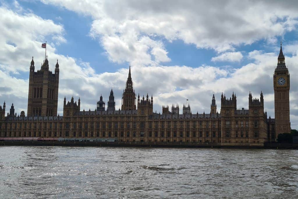 Parliament buildings on a river with a tall clock tower.