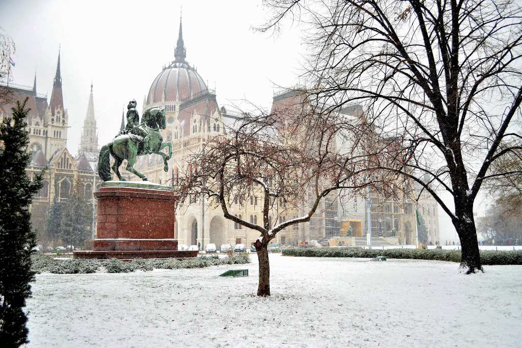 Snowy white park with horse monument and European city in the distance.