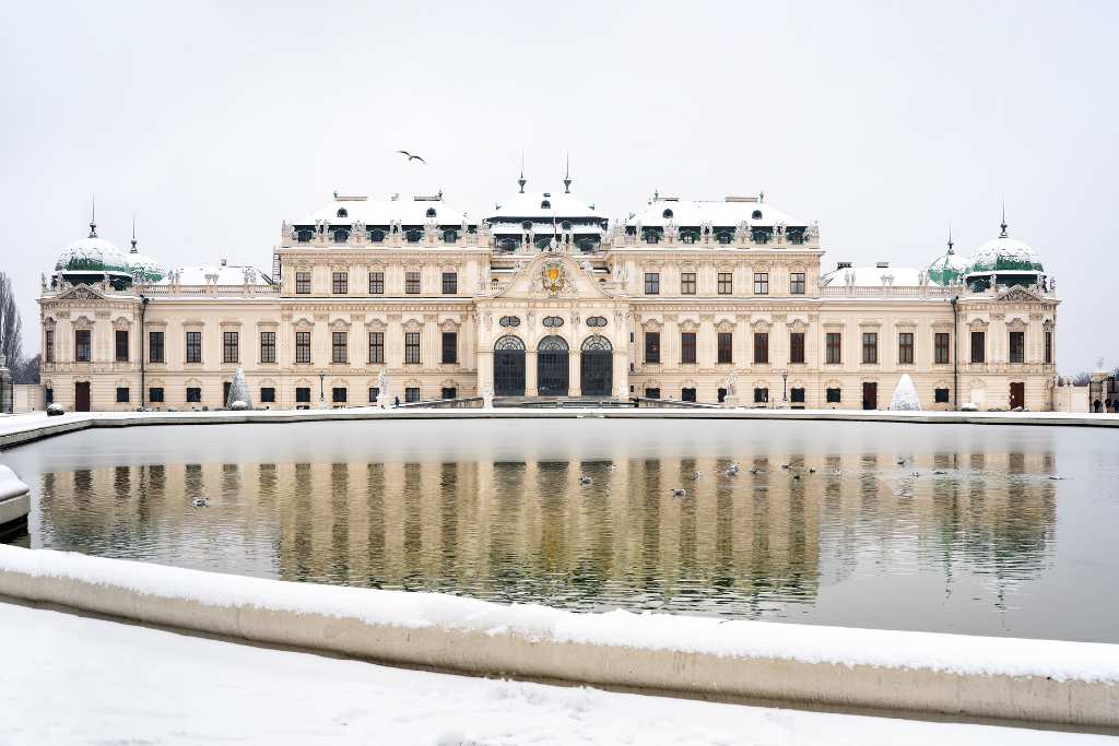 A grand palace covered in snow set behind a pond. A typical site in Vienna in winter.