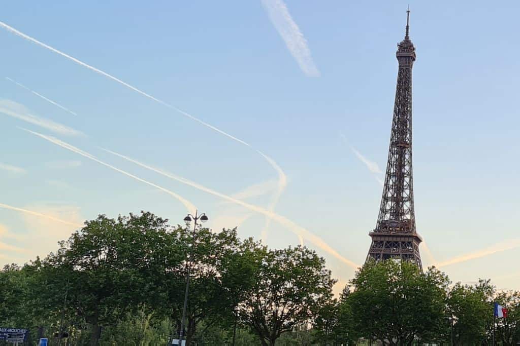 Iconic tall metal French tower surrounded by trees against a blue sky.