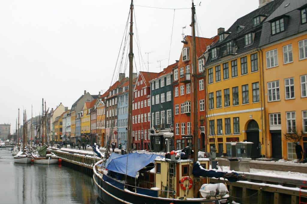 A row of colourful houses lining a canal with boats with snow in winter.