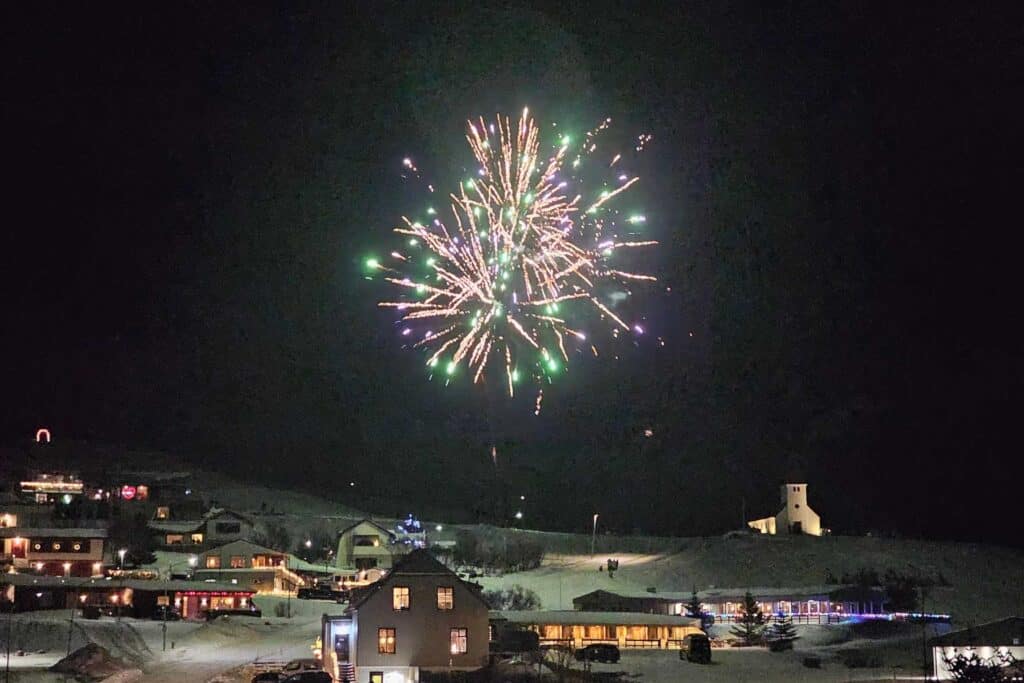 Pink and green fireworks in the night sky over a snowy town in Iceland.