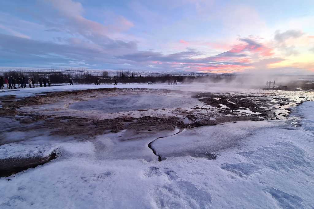 Snow surrounding a steaming pool of water.