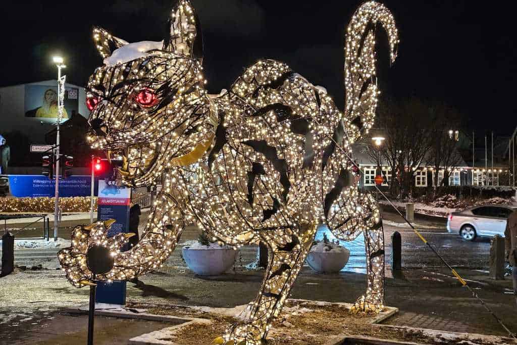 A large cat sculpture lit up with white lights on a street.