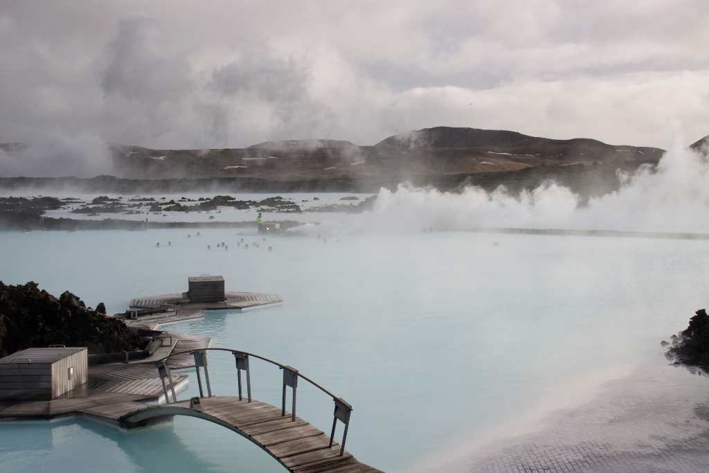 Steaming geothermal pool with cloudy blue water and a wooden bridge.