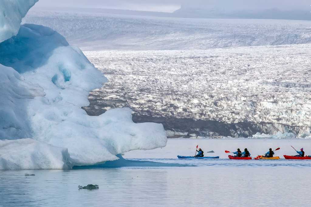 A group kayaking on a lake near icebergs in Iceland. 