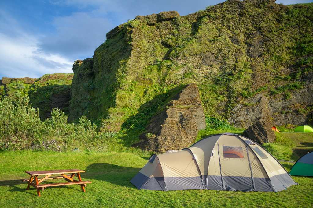 Tents in a grassy campsite with a cliff.